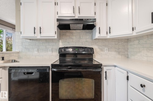 Kitchen featuring white cabinetry with matte black hardware, a black electric range with an overhead vent, a stainless steel sink, and white subway tile backsplash - 16811 91 Street, Edmonton, AB 