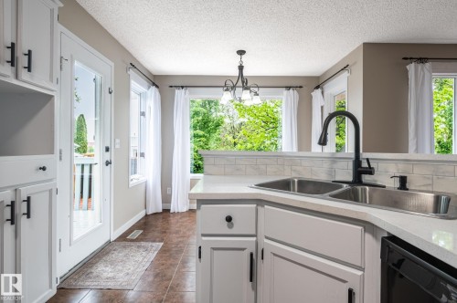 Kitchen featuring white cabinetry with matte black hardware, double basin stainless steel sink with a matte black faucet, light-toned countertops, and a subway tile backsplash - 16811 91 Street, Edmonton, AB 