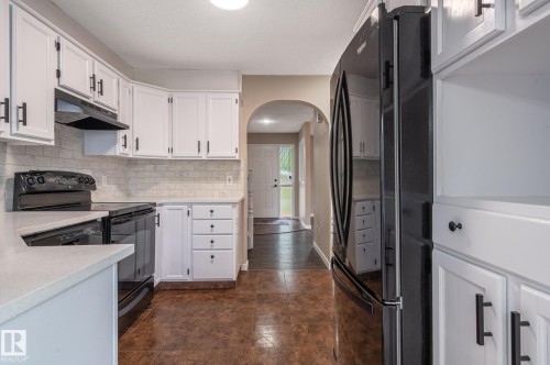 Kitchen featuring white cabinetry with matte black hardware, light-toned countertops, a subway tile backsplash, and dark-finish appliances - 16811 91 Street, Edmonton, AB 