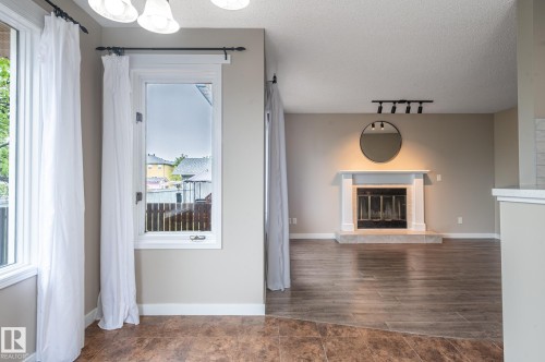 Living area featuring a white mantel fireplace with a dark tile hearth, wood-finish flooring, and a track lighting fixture - 16811 91 Street, Edmonton, AB 