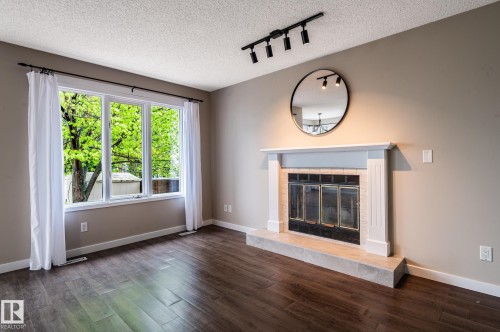 Living area featuring a fireplace with a light-colored mantel and hearth, dark wood-finish flooring, a large multi-pane window, track lighting, and neutral wall paint - 16811 91 Street, Edmonton, AB 