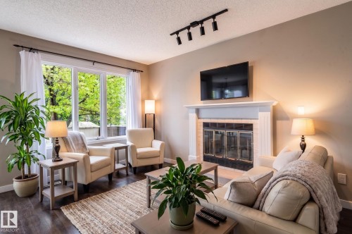 Living room featuring a prominent fireplace with a classic mantel, dark wood-finish flooring, and a large multi-pane window - 16811 91 Street, Edmonton, AB 
