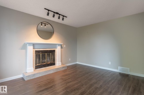 Living area featuring a fireplace with a white mantel, dark wood-finish flooring, light gray walls, and a track lighting fixture - 16811 91 Street, Edmonton, AB 