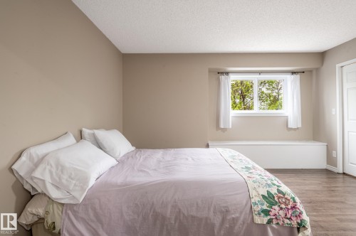 Spacious bedroom featuring wood-finish flooring, neutral wall tones, and a window with a built-in window seat - 16811 91 Street, Edmonton, AB 