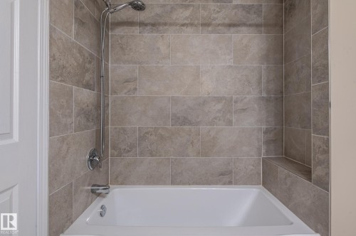 Bathtub with an integrated shower system, featuring textured rectangular tile surround, a built-in shower niche, and polished chrome fixtures - 16811 91 Street, Edmonton, AB 
