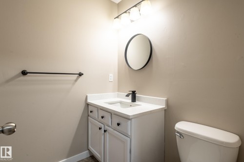 Bathroom vanity with a white countertop and integrated sink, matte black faucet, and a circular mirror - 16811 91 Street, Edmonton, AB 