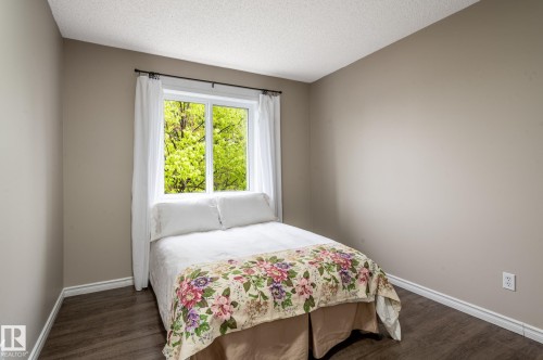 Light-filled room featuring a large window, neutral wall paint, wood-finish flooring, white baseboards, and a textured ceiling - 16811 91 Street, Edmonton, AB 