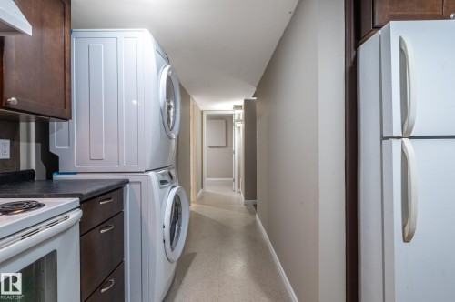 Compact kitchen area featuring a white electric range, dark wood-finish cabinetry, and a stacked white washer and dryer unit - 16811 91 Street, Edmonton, AB 