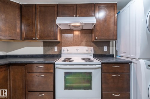 Kitchen area featuring dark wood-finish cabinetry, dark countertops, tile backsplash, and a white electric range with overhead ventilation - 16811 91 Street, Edmonton, AB 