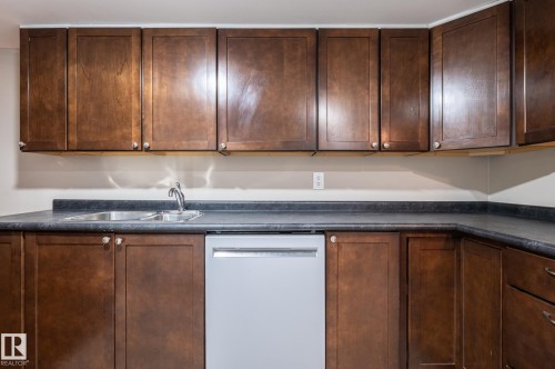 Kitchen featuring ample wood-finish cabinetry, dark countertops, and a double basin stainless steel sink with a chrome faucet - 16811 91 Street, Edmonton, AB 