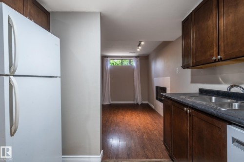 Compact kitchen area featuring wood-finish cabinetry, a double basin sink with a chrome faucet, and dark countertops - 16811 91 Street, Edmonton, AB 