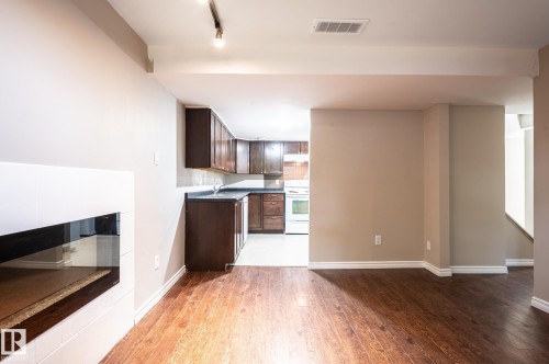 Open-concept living area featuring wood-finish flooring, a contemporary built-in fireplace with a glass front, and a track lighting fixture - 16811 91 Street, Edmonton, AB 