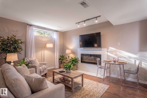 Living area with wood-finish flooring, a wall-mounted fireplace with white tile surround, and an egress window - 16811 91 Street, Edmonton, AB 