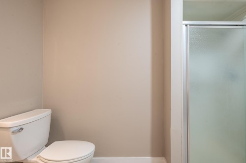 Bathroom featuring a white toilet, neutral wall paint, and a shower enclosure with frosted glass and a silver-toned frame - 16811 91 Street, Edmonton, AB 