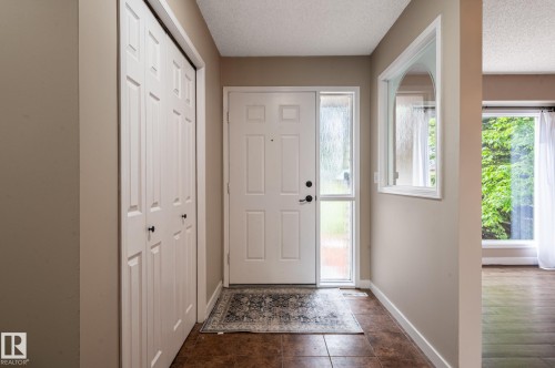 Entryway featuring a white door with a frosted sidelight, brown tile flooring, and bi-fold closet doors - 16811 91 Street, Edmonton, AB 