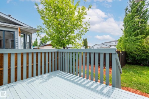 Spacious outdoor deck with painted wood flooring and railing, overlooking a verdant lawn and mature trees - 16811 91 Street, Edmonton, AB 