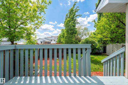 Deck with light blue wood-finish railing and stairs overlooking a backyard with green grass, mature trees, and red mulch - 16811 91 Street, Edmonton, AB 