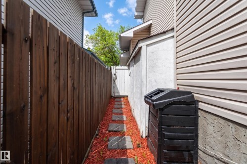 Side yard featuring a wood privacy fence, stepping stones, and red mulch landscaping - 16811 91 Street, Edmonton, AB 