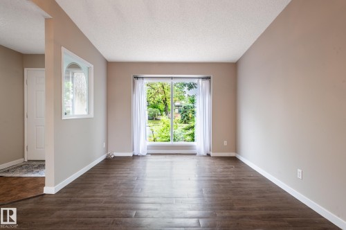 Spacious room featuring wood-finish flooring, a large sliding glass door, white trim, and neutral paint - 16811 91 Street, Edmonton, AB 