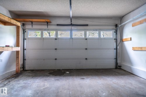 Attached garage featuring a sectional overhead door with upper window panels, concrete flooring, and built-in wood shelving - 16811 91 Street, Edmonton, AB 