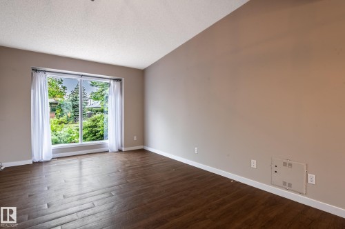 Spacious room featuring a large window, wood-finish flooring, neutral wall tones, white baseboards, and a textured ceiling - 16811 91 Street, Edmonton, AB 