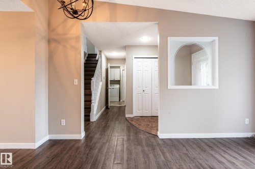 Expansive interior featuring wood-finish flooring, a contemporary chandelier, a staircase with white spindles, and a built-in arched pass-through window - 16811 91 Street, Edmonton, AB 