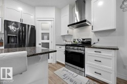 Modern kitchen featuring white shaker cabinetry, dark granite countertops, stainless steel appliances, a subway tile backsplash, and light wood-finish flooring - 