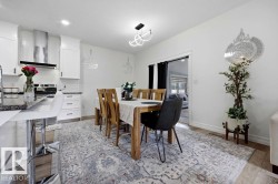 Open-concept kitchen and dining area featuring white cabinetry, dark countertops, wood-finish flooring, a contemporary chandelier, and a stainless steel range hood - 
