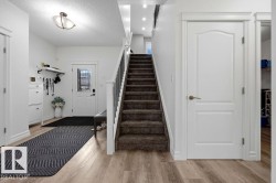 Entryway featuring wood-finish flooring, a carpeted staircase with a white and black railing, and white interior doors with bronze hardware - 