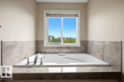 Built-in soaking tub with chrome fixtures, surrounded by large format tile in varying shades of gray, and a window with blinds - 