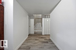 Hallway featuring wood-finish flooring, white painted walls, and a staircase with wood treads and a metal handrail - 