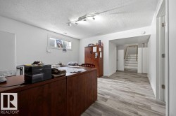 Spacious room featuring light wood-finish flooring, white walls, a track lighting fixture, and a window with horizontal blinds - 