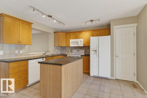 Kitchen featuring wood-finish cabinetry, dark countertops, a central island, and ceramic tile flooring - 12215 18 Avenue Sw, Edmonton, AB 