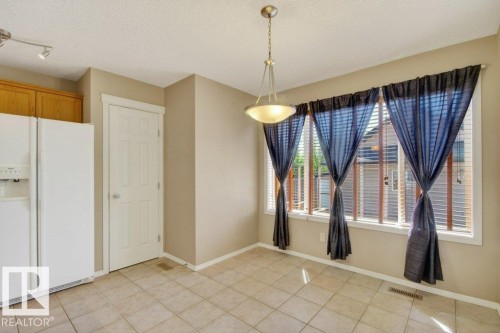 Dining area featuring a contemporary pendant light fixture, extensive window wall, and neutral-toned tile flooring - 12215 18 Avenue Sw, Edmonton, AB 