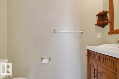 Bathroom vanity featuring a wood-finish cabinet with decorative detailing, an integrated sink, and a framed mirror - 12215 18 Avenue Sw, Edmonton, AB 