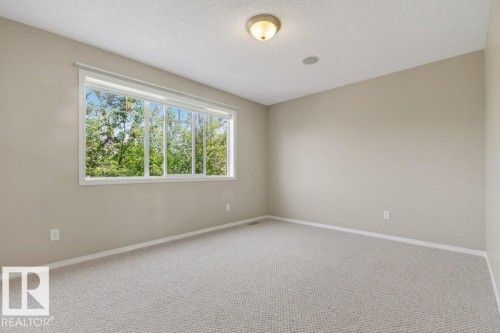 Carpeted room featuring a large window with white trim, a flush-mount ceiling light, and light neutral wall paint - 12215 18 Avenue Sw, Edmonton, AB 