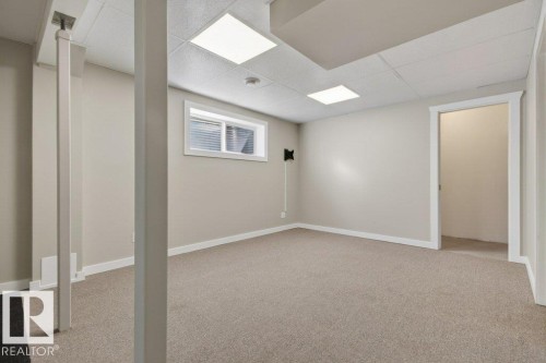 Open finished room featuring neutral carpet flooring, a drop ceiling with recessed lighting, a horizontal window with blinds, and painted walls - 12215 18 Avenue Sw, Edmonton, AB 
