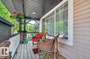 Covered front porch featuring wood-finish decking, stone-clad pillars, white balusters, and a paneled ceiling with recessed lighting - 12215 18 Avenue Sw, Edmonton, AB 