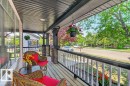 Covered front porch featuring wood-finish decking, dark railing with white spindles, and stone-clad support pillars - 12215 18 Avenue Sw, Edmonton, AB 