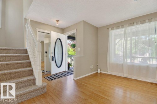Entryway featuring a carpeted staircase with white balusters, wood-finish flooring, and a front door with an oval glass insert - 12215 18 Avenue Sw, Edmonton, AB 