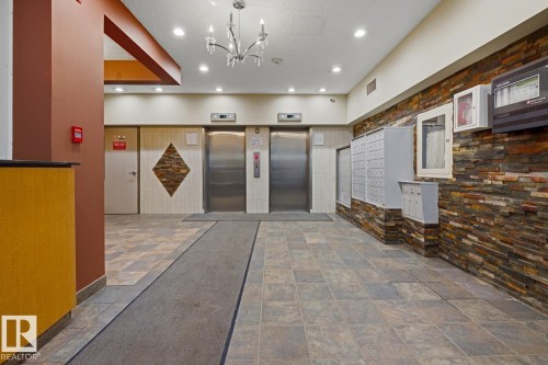 Building lobby featuring dual stainless steel elevators, slate-look tile flooring, and a stone accent wall - 703 9710 105 Street, Edmonton, AB 
