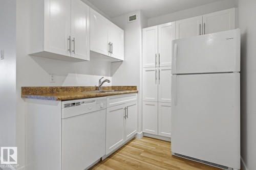Kitchen featuring white cabinetry, a light wood-finish floor, a refrigerator, a dishwasher, and a sink with a chrome faucet - 703 9710 105 Street, Edmonton, AB 