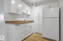 Kitchen featuring white cabinetry, a light wood-finish floor, a refrigerator, a dishwasher, and a sink with a chrome faucet - 703 9710 105 Street, Edmonton, AB 