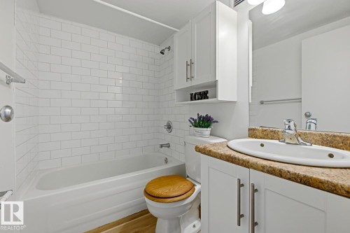 Full bathroom featuring a white subway tile tub surround, white vanity with integrated sink, and an earthy-toned countertop - 703 9710 105 Street, Edmonton, AB 