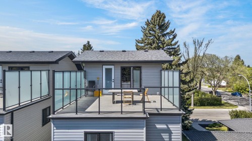 Rooftop deck featuring gray composite decking, black metal railings with clear and frosted glass panels, and direct access to interior spaces through a white door and sliding glass door - 8809 148 Street, Edmonton, AB - Outdoor