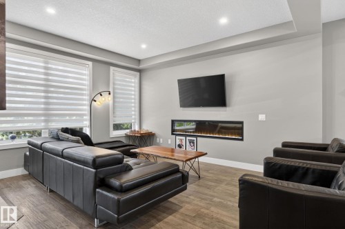 Living space featuring wood-finish flooring, a linear electric fireplace, recessed ceiling lighting, and a tray ceiling - 8809 148 Street, Edmonton, AB - Indoor Photo Showing Living Room With Fireplace