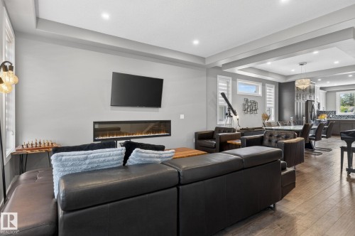Spacious living area featuring wood-finish flooring, an electric fireplace with mounted television, and recessed lighting - 8809 148 Street, Edmonton, AB - Indoor Photo Showing Living Room With Fireplace