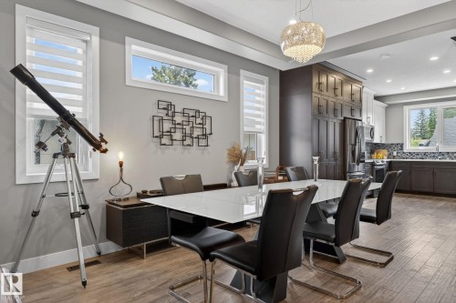 Open-concept dining area featuring wood-finish flooring, a contemporary chandelier, multiple windows with blinds, a built-in dark wood storage unit, and recessed lighting - 8809 148 Street, Edmonton, AB - Indoor Photo Showing Dining Room