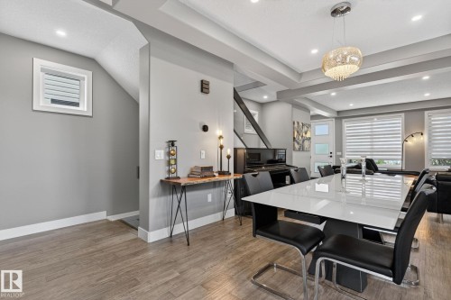 Open-concept living area featuring wood-finish flooring, a contemporary chandelier, recessed lighting, a white panel door, and large windows with horizontal blinds - 8809 148 Street, Edmonton, AB - Indoor Photo Showing Dining Room