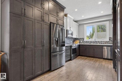 Spacious kitchen featuring extensive floor-to-ceiling cabinetry, stainless steel appliances, mosaic tile backsplash, wood-finish flooring, and recessed lighting - 8809 148 Street, Edmonton, AB - Indoor Photo Showing Kitchen With Upgraded Kitchen